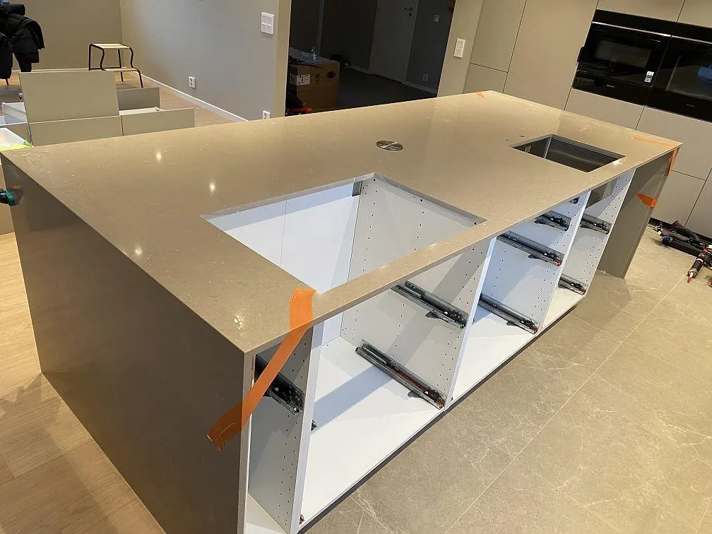 Køkkenø i poleret Silestone Coral Clay, varm taupe kvartskomposit, med öppet hällurtag og rostfri vask i ett køkken under montering i Malmö.