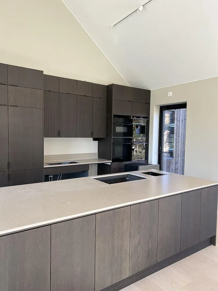 Køkkenbordplade og køkkenø i mat Silestone Coral Clay, gråbeige kvartskomposit med förberedda öppningar og låg stänkkant i ett køkken i Rö.