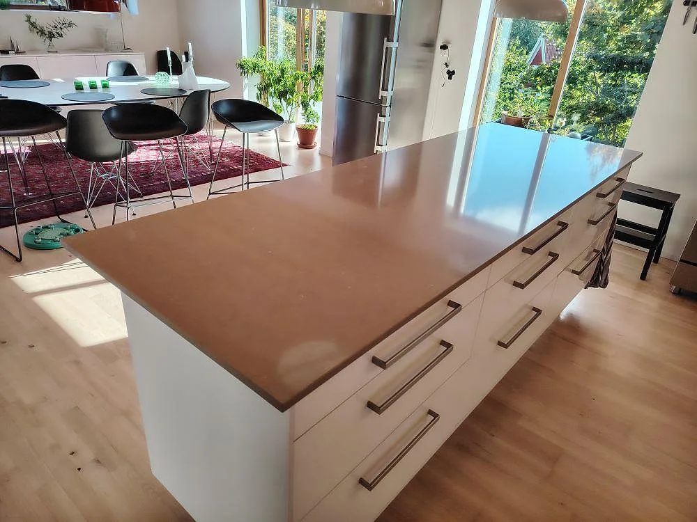 Køkkenø i lerbeige Silestone Coral Clay, poleret kompositsten, monteret på vita lådskåp i ett öppet køkken i Saltsjöbaden.