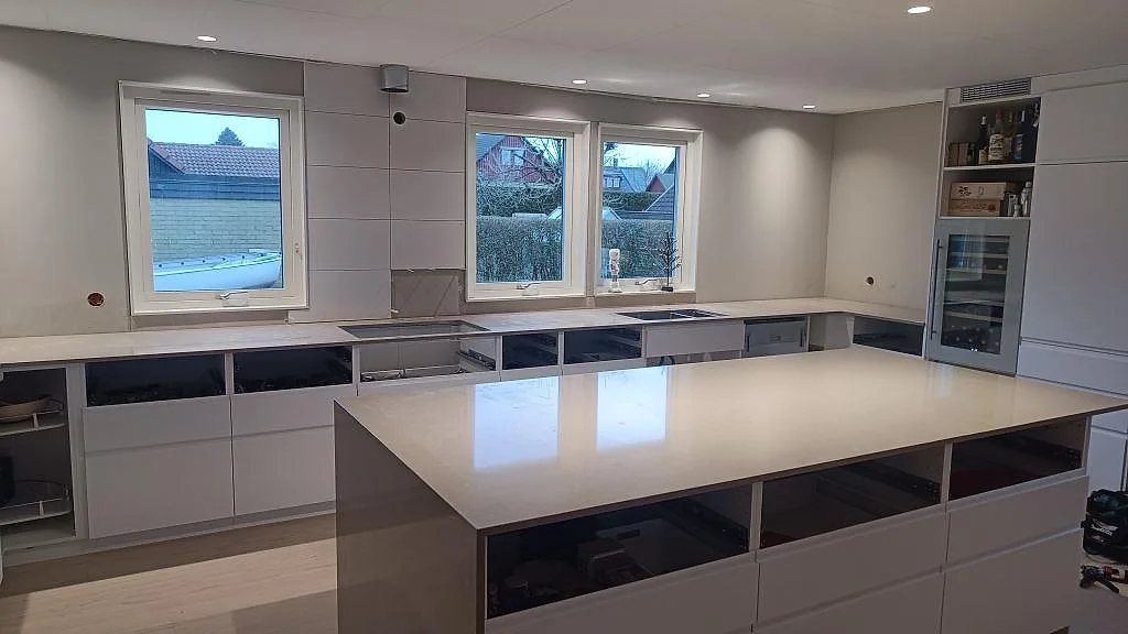 Køkkenbordplade i poleret Silestone Coral Clay, lys kvartskomposit, med stor køkkenø og väggbänkar i ett køkken i Sjöbo.
