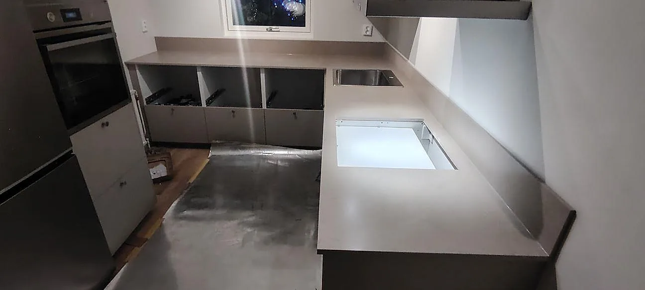 Køkkenbordplade i mat grå Silestone Coral Clay, kvartskomposit, med uppvikt stänkkant og synlig diskhozon i ett køkken under montering i Södertälje.