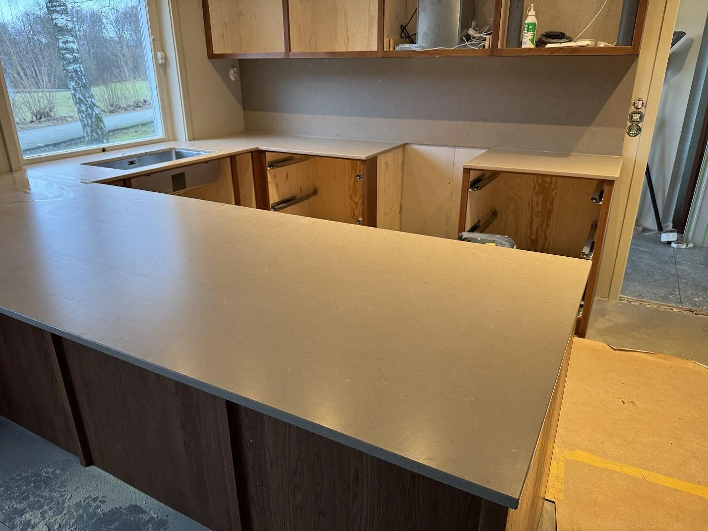 Køkkenbordplade og køkkenø i mat Silestone Coral Clay, 20 mm kvartskomposit, med rostfri vask og stænkplade i ett køkken i Sösdala.