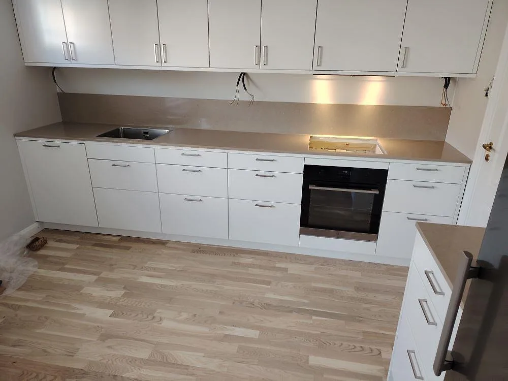 Køkkenbordplade i Silestone Coral Clay, poleret varm gråbeige kvartskomposit, med rostfri vask, förberett hälläge og matchande stænkplade i ett vitt køkken i Täby.