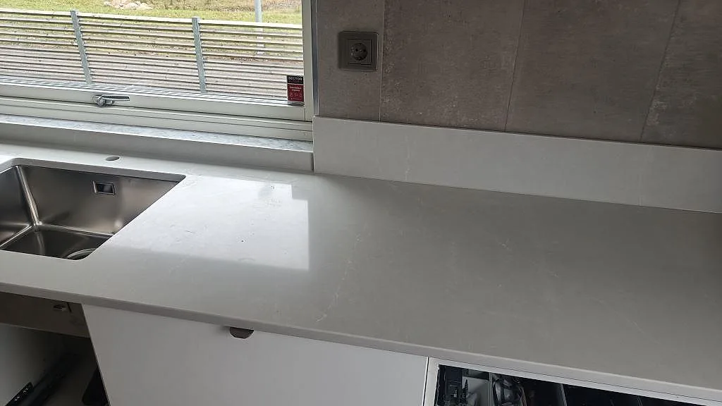 Køkkenbordplade i poleret Silestone Desert Silver, grå kvartskomposit med rostfri vask og lavt stænkplade i ett køkken i Ängelholm.
