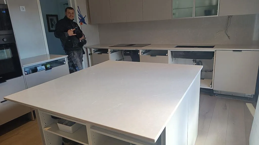 Køkkenbordplade og stort køkkenø i Silestone Desert Silver, varmgrå kvartskomposit med mat overflade, i ett køkken under montering i Helsingborg.