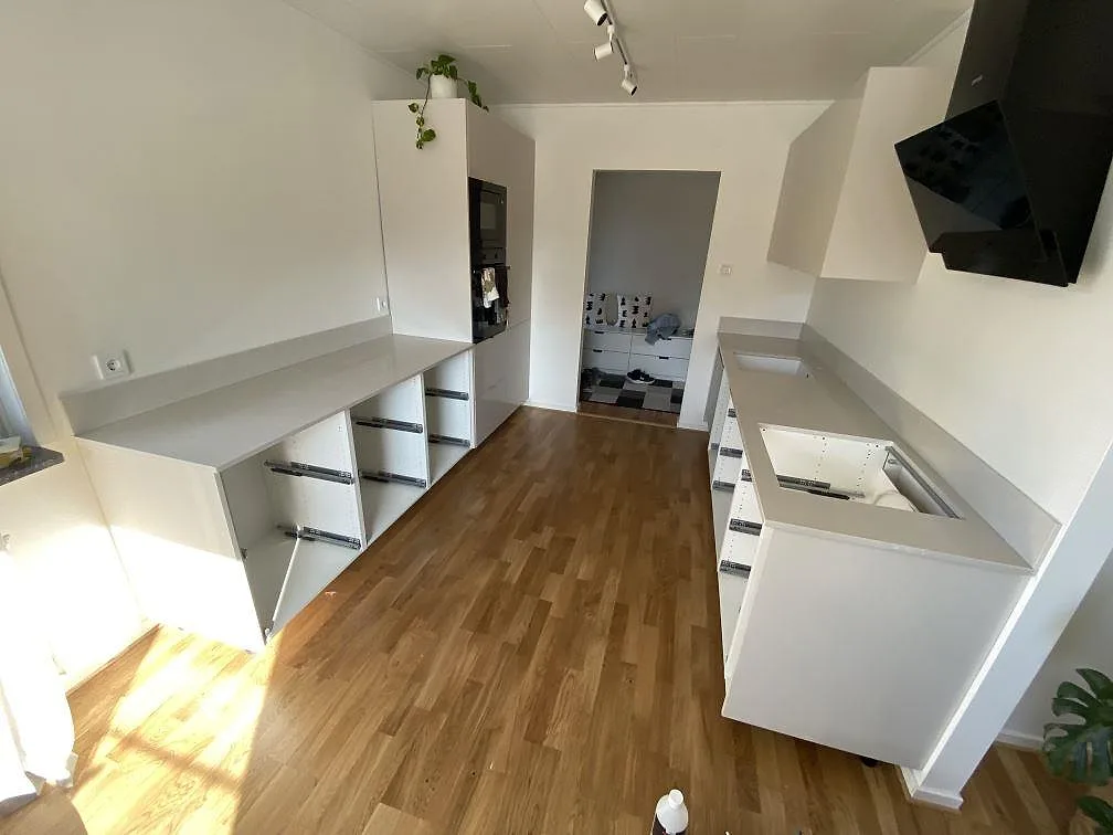 Køkkenbordplader i poleret Silestone Desert Silver med uppvikt stænkplade längs två vægge i ett køkken i Ingelstad.