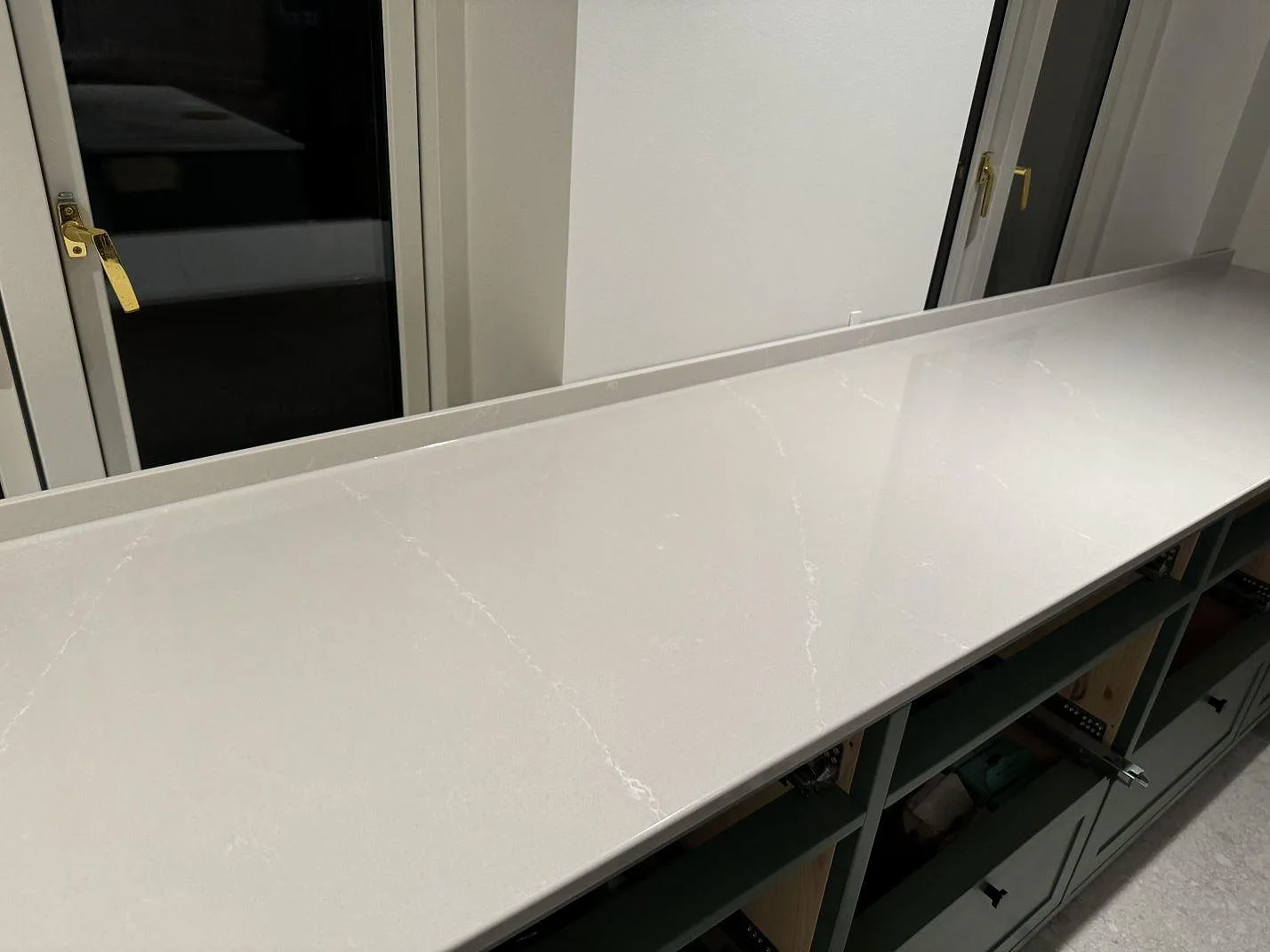 Lang køkkenbordplade i poleret Silestone Desert Silver, lys kvartskomposit med låg stänkkant under montering i Klagshamn.