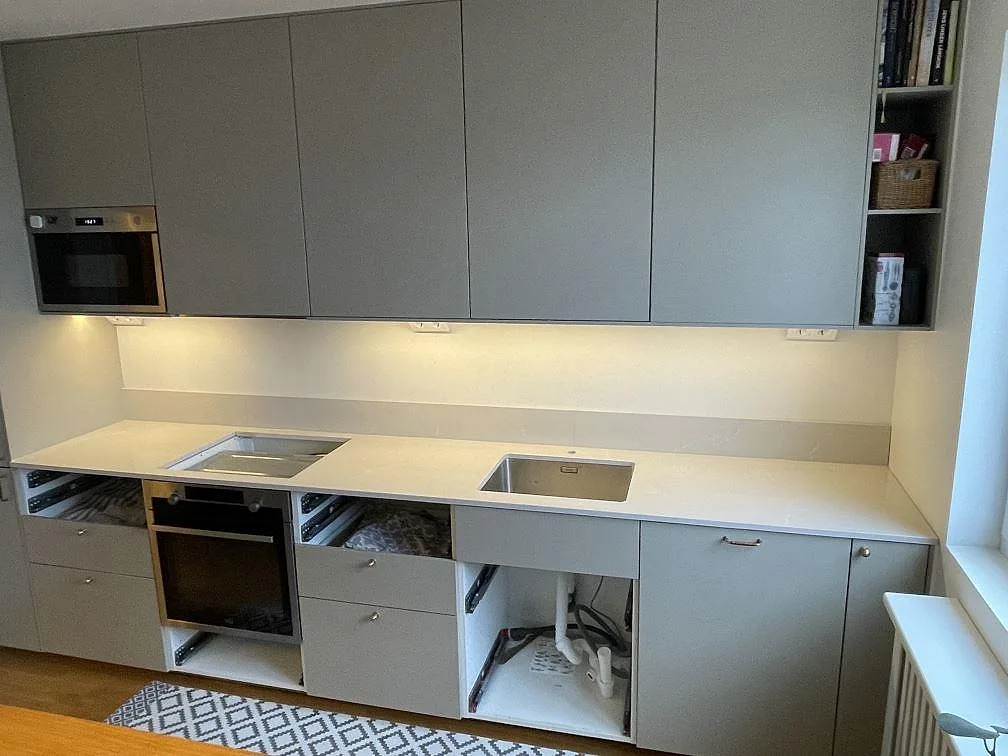 Køkkenbordplade i lys Silestone Desert Silver, poleret, med låg stänkkant og hällöppning i ett køkken i Lidingö.