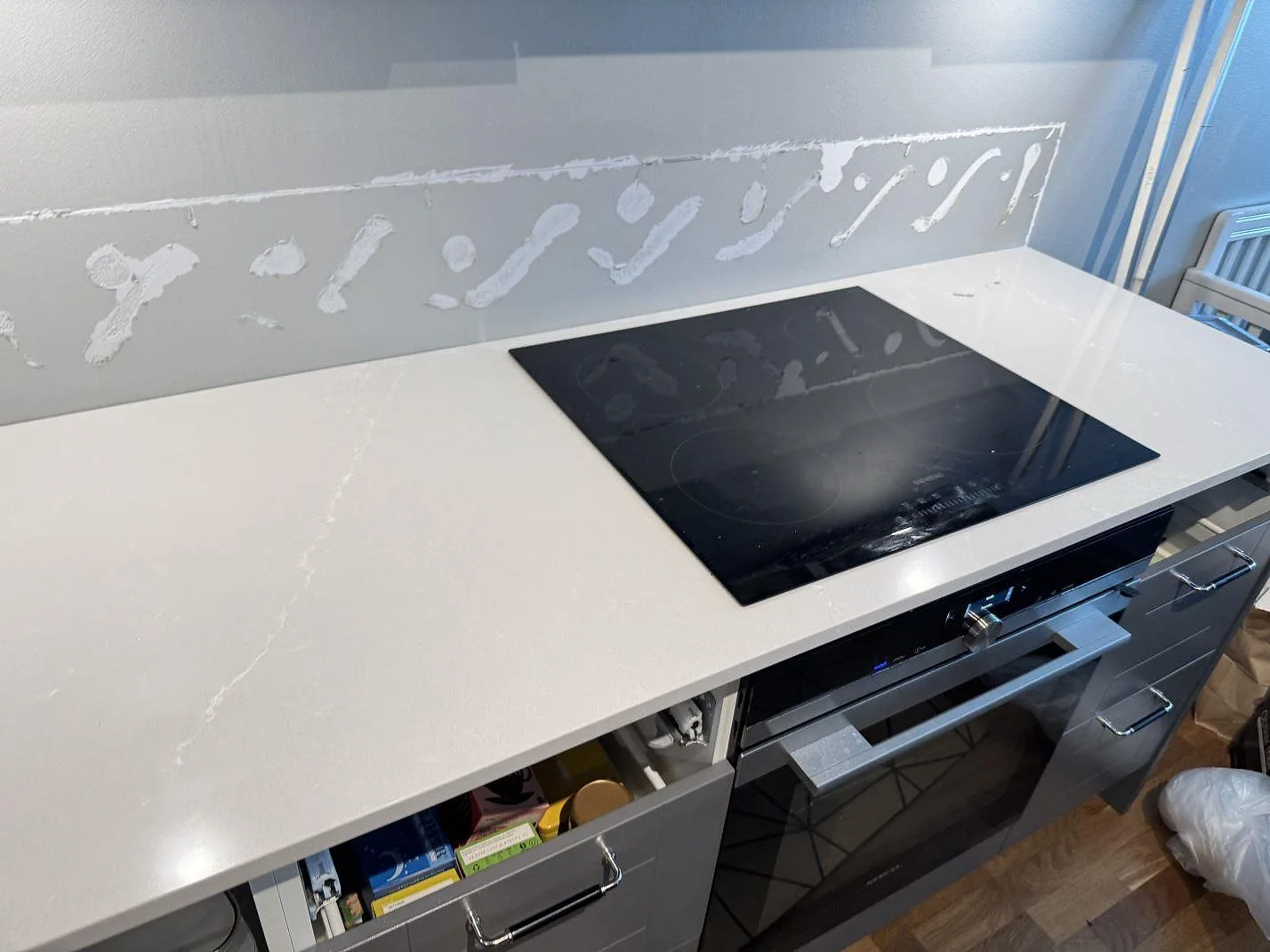 Køkkenbordplade i poleret Silestone Desert Silver med sort kogeplade og lyse vener i ett køkken i Limhamn.