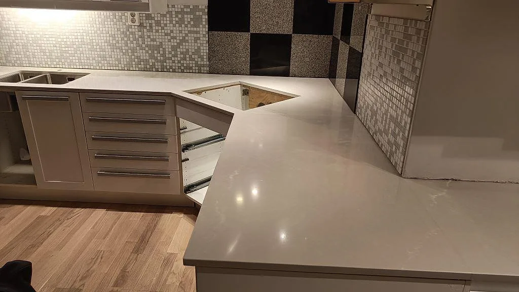Køkkenbordplade i poleret Silestone Desert Silver komposit i ett L-format køkken i Lund, med diskhozon og öppning i arbetsytan.