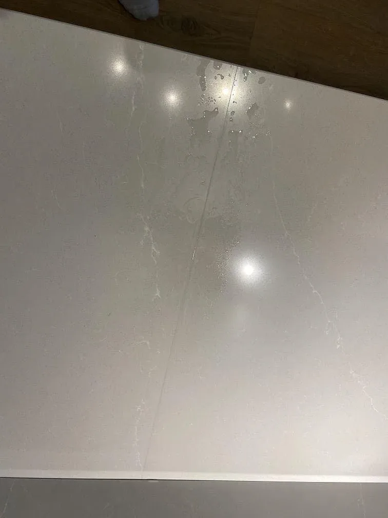 Køkkenbordplade i Silestone Desert Silver, poleret gråbeige kvartskomposit, monteret i ett køkken i Malmö med gråröna skabe og waterfall-gavel, fotograferad under montering.
