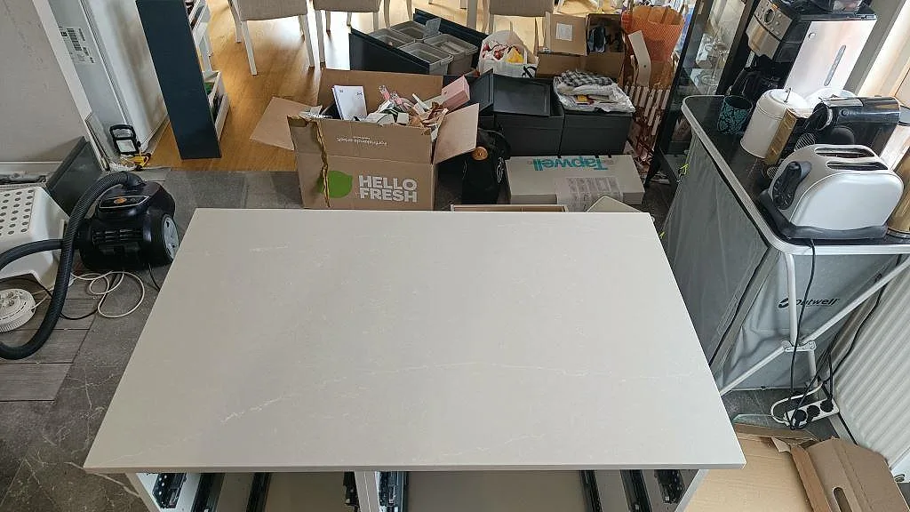 Køkkenø i varmt greige Silestone Desert Silver, poleret kvartskomposit, monteret i ett køkken under installation i Sandared.