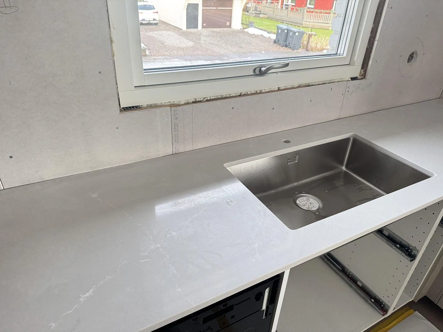 Køkkenbordplade i poleret Silestone Desert Silver, komposit, med vask vid vindue i ett køkken i Sandared.