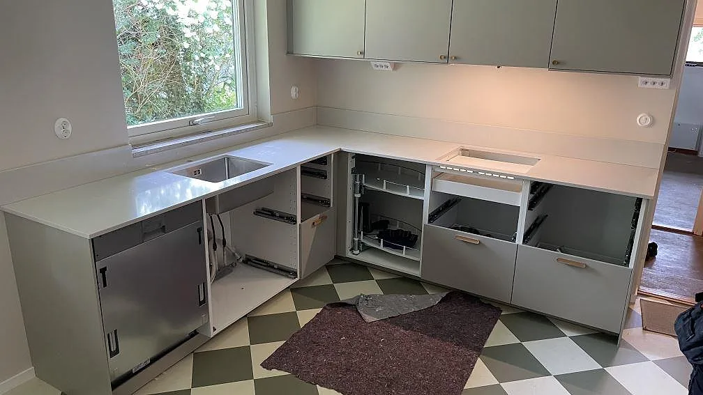 L-formad køkkenbordplade i poleret Silestone Desert Silver, kvartskomposit, med låg stänkkant og rostfri vask i ett køkken i Skanör.