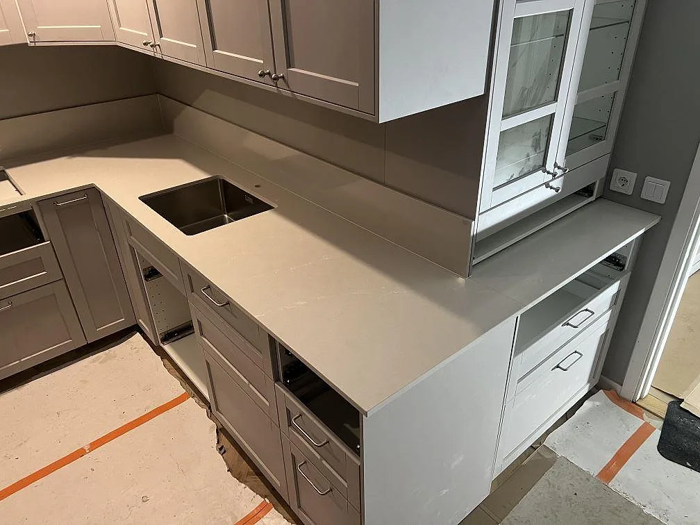 Køkkenbordplade i poleret Silestone Desert Silver, lys gråbeige komposit, med synlig vask og låg stänkkant i ett køkken i Solna.