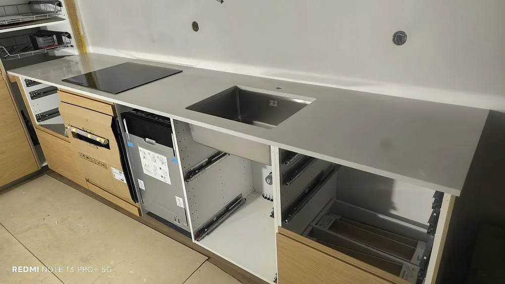 Køkkenbordplade i lys Silestone Desert Silver, poleret kvartskomposit, med rostfri vask og kogeplade under montering i Stockholm.