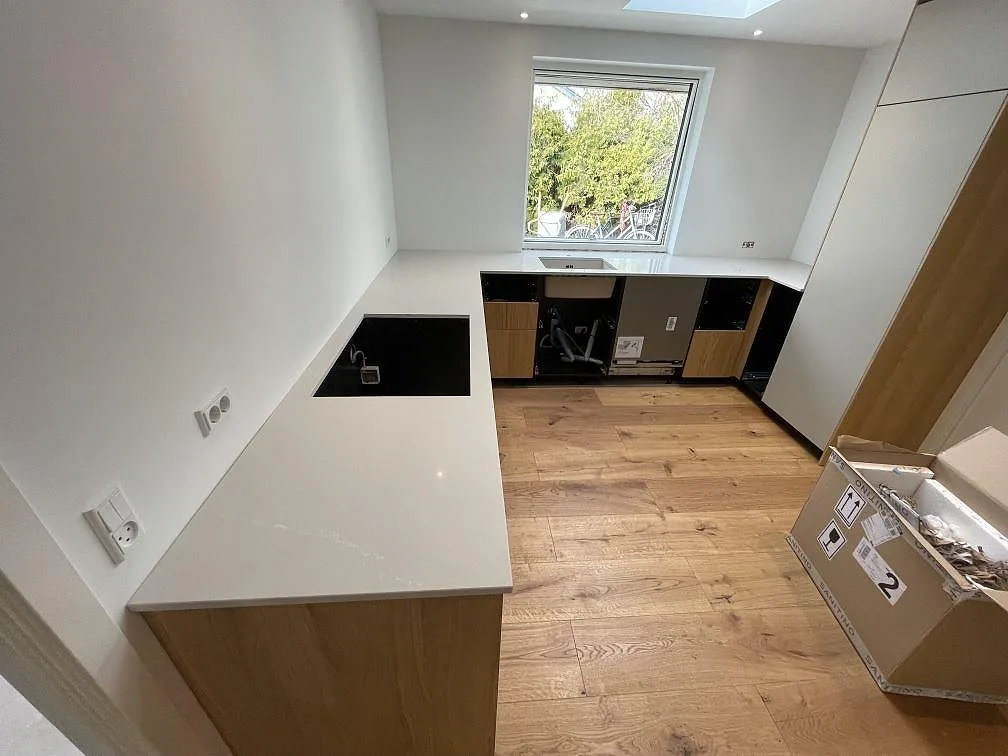 Køkkenbordplade i Silestone Desert Silver, ljust grå poleret kvartskomposit, med sort underlimmad vask og plats for induktionshäll i en vinklad köksuppställning i Svendborg.
