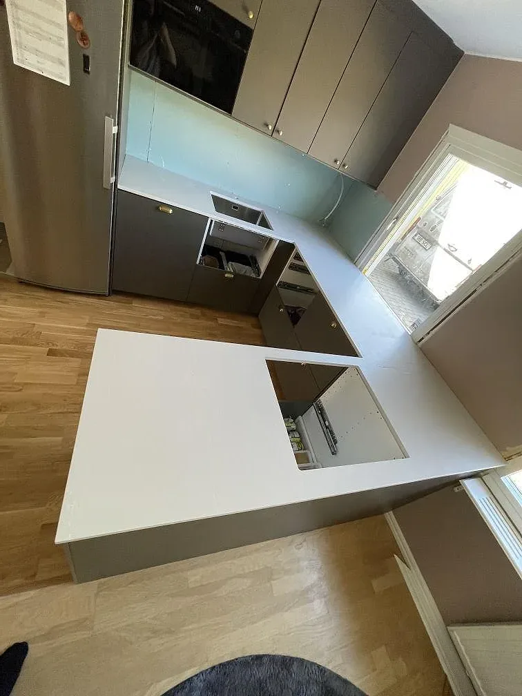 Køkkenbordplade i Silestone Desert Silver, mat gråbeige komposit med 20 mm tykkelse, monteret i L-form med køkkenø i ett køkken under montering i Täby.
