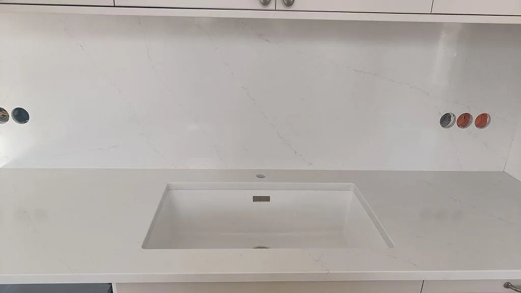 Poleret Silestone Eternal Statuario som Bordplade og stænkplade vid vask i ett vitt køkken i Limhamn.