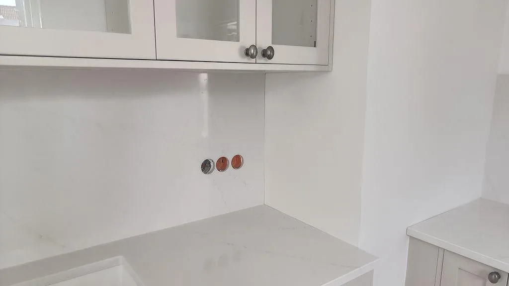 Køkkenbordplade og väggskiva i poleret Silestone Eternal Statuario rundt om diskhozonen i ett ljust køkken i Limhamn.