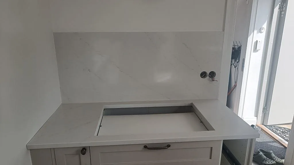 Poleret Silestone Eternal Statuario med stor hällöppning og väggskiva i en köksnisch under montering i Limhamn.