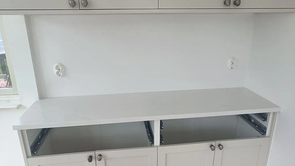 Lige køkkenbordplade i poleret Silestone Eternal Statuario på vita skabe i ett køkken under montering i Limhamn.
