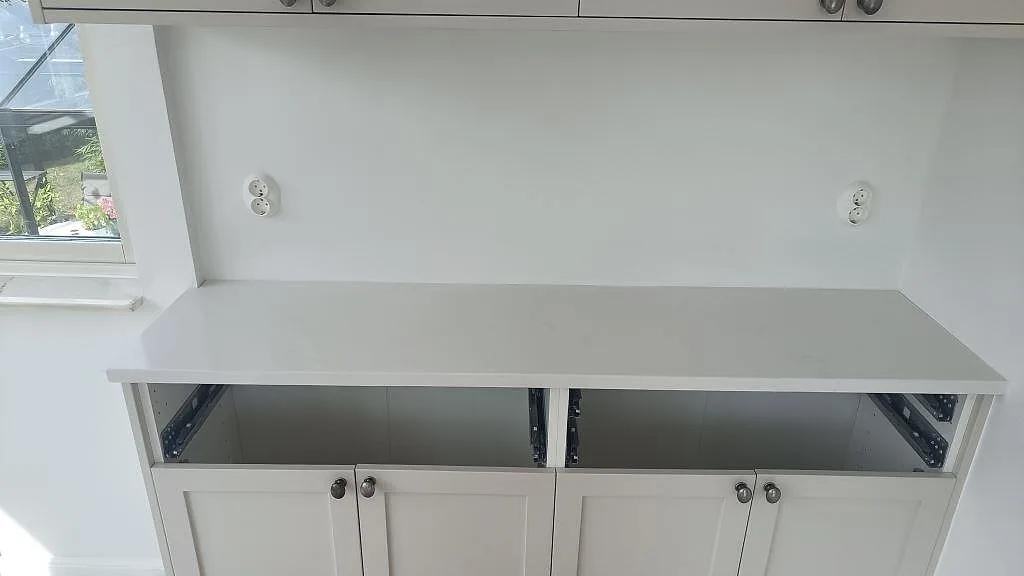 Lang bänkyta i hvid Silestone Eternal Statuario, poleret, intill vindue og vita köksstommar i Limhamn.