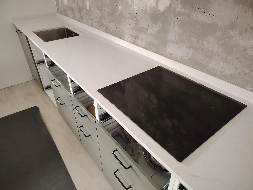 Närbild af poleret Silestone Eternal Statuario som køkkenbordplade med kogeplade, vask og blød grå åretegning under montering i Stockholm.
