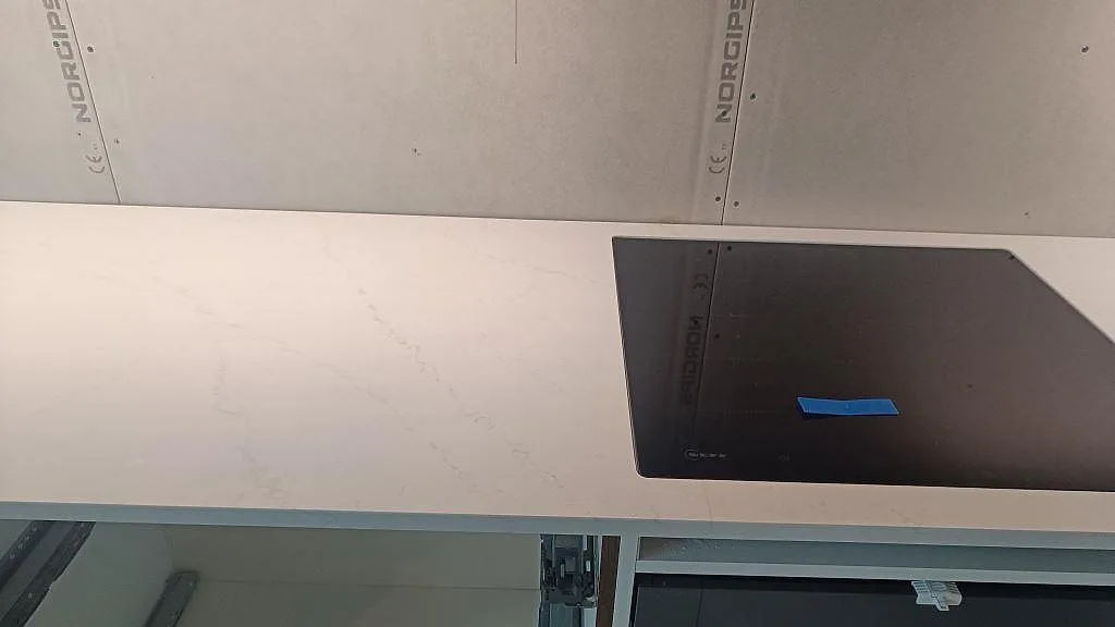 Detalj af poleret Silestone Eternal Statuario Bordplade med induktionshäll og diskret grå åretegning i Varberg.