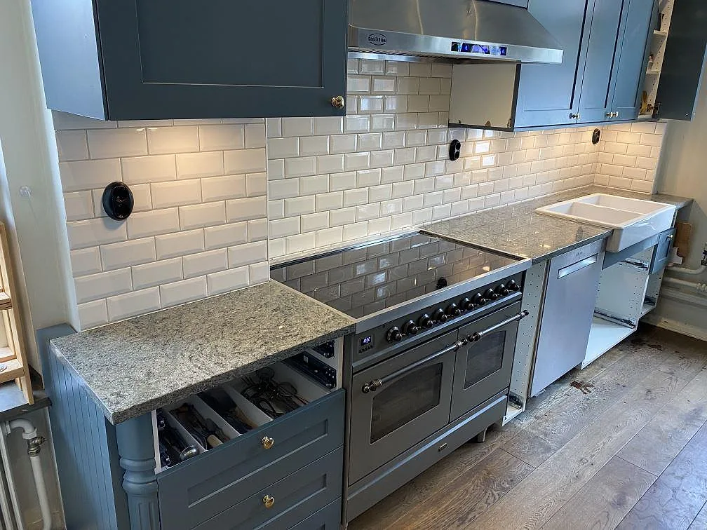 Køkkenbordplade i poleret Silestone Jardin Emerald kompositsten med grågrön åretegning, fristående komfur og hvid vask i ett køkken i Malmö.