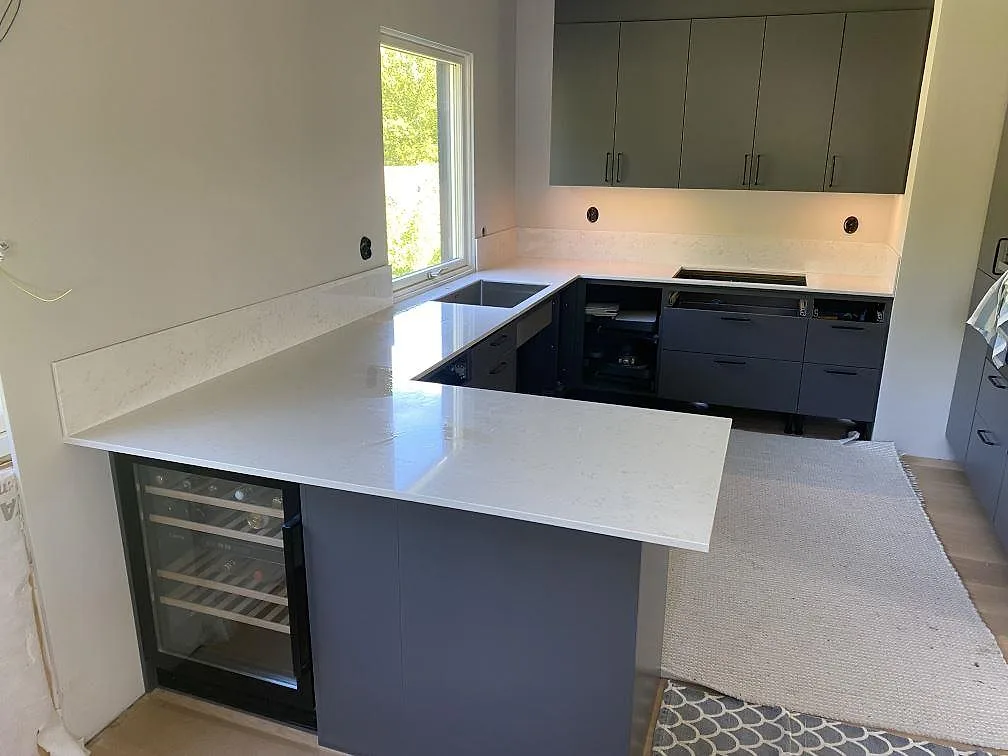 Køkkenbordplade i poleret Silestone Lagoon, lys kvartskomposit med grå åretegning, monteret som L-formad bordplade og framskjutande arbetsyta i ett køkken i Hovås.