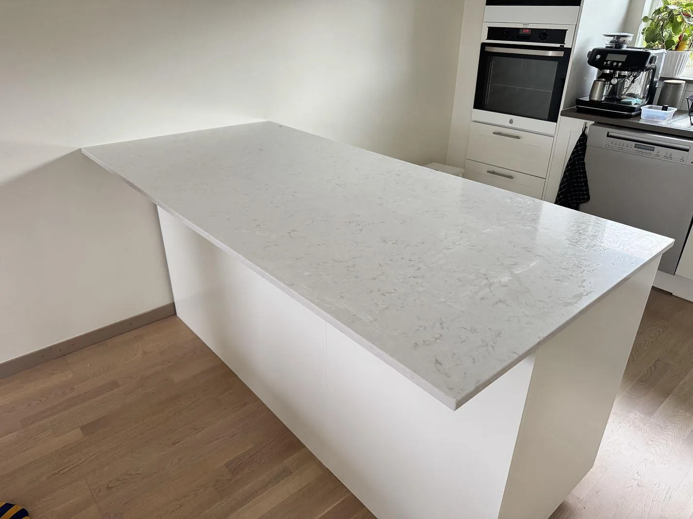 Køkkenø med køkkenbordplade i poleret Silestone Lagoon, lys kvartskomposit med grå åretegning, i ett køkken i Limhamn.