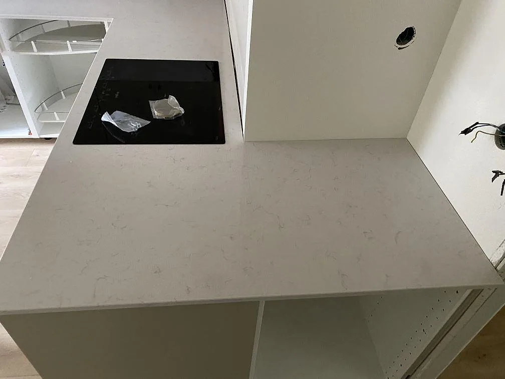 Køkkenbordplade i krämvit Silestone Lagoon, poleret, med sort induktionshäll infälld i köksön i ett køkken under montering i Malmö.