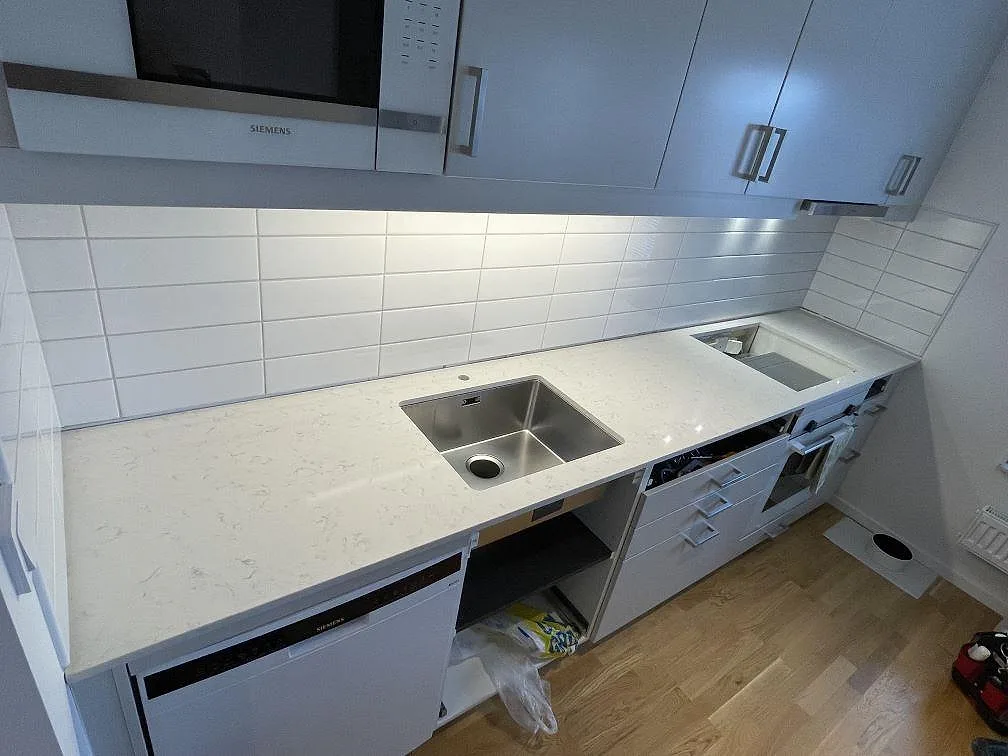 Køkkenbordplade i lys Silestone Lagoon, poleret komposit, med underlimmad rostfri vask og hvid kakelvägg i ett køkken i Trosa.