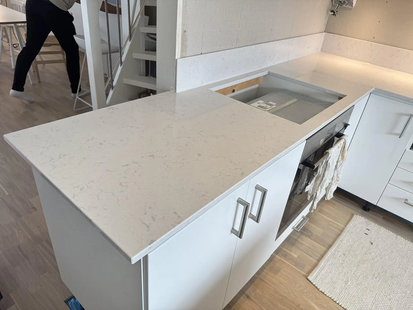 Poleret køkkenbordplade i Silestone Lagoon med hällöppning, låg väggsten og vita skabe i ett køkken i Växjö.