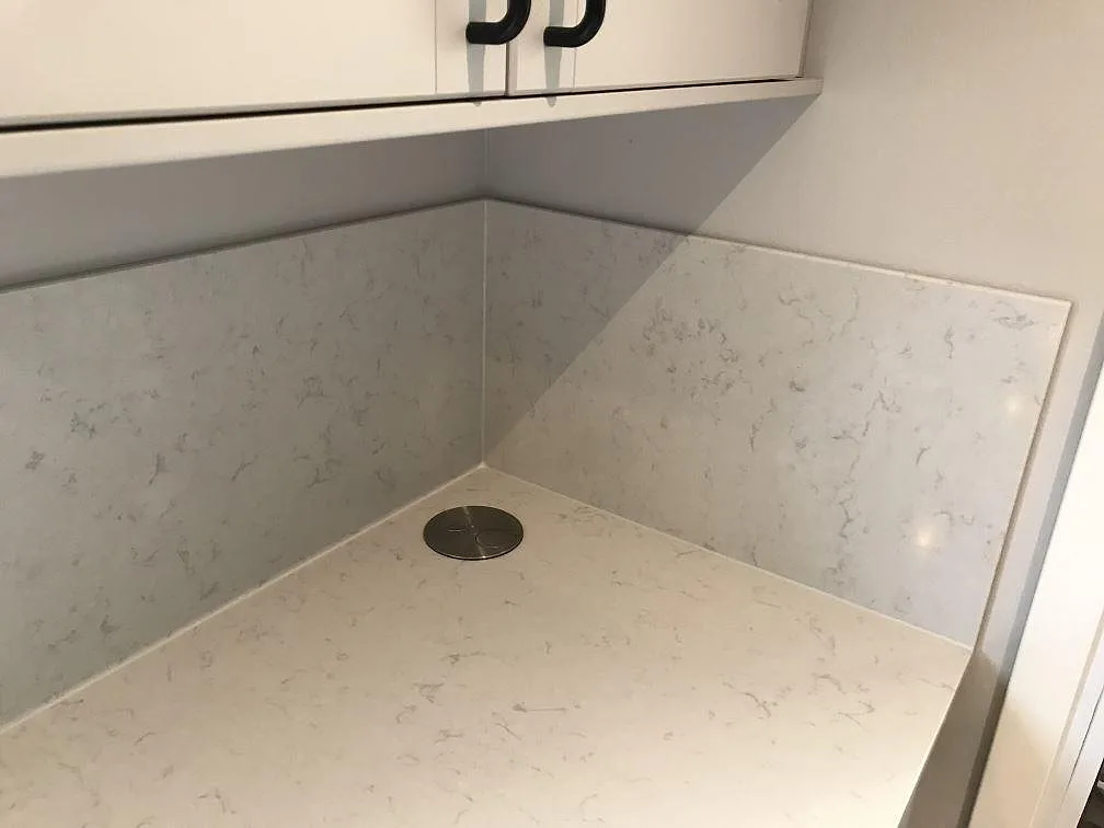 Køkkenbordplade i krämvit Silestone Lagoon, poleret, med heltäckande stänkväggar i hjørner og infällt rundt om eluttag i ett køkken i Veberöd.