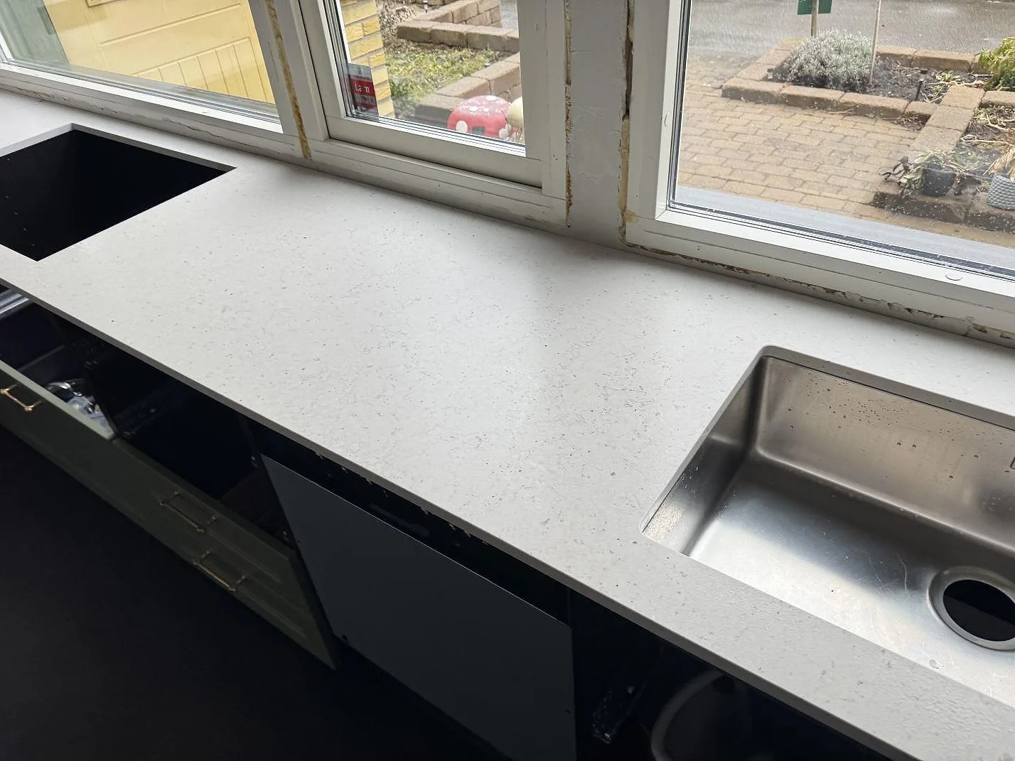 Køkkenbordplade i krämvit Silestone Lime Delight, mat Mocka-finish, längs vindue i ett køkken i Åkarp med underlimmad rostfri vask og salviegröna fronter.