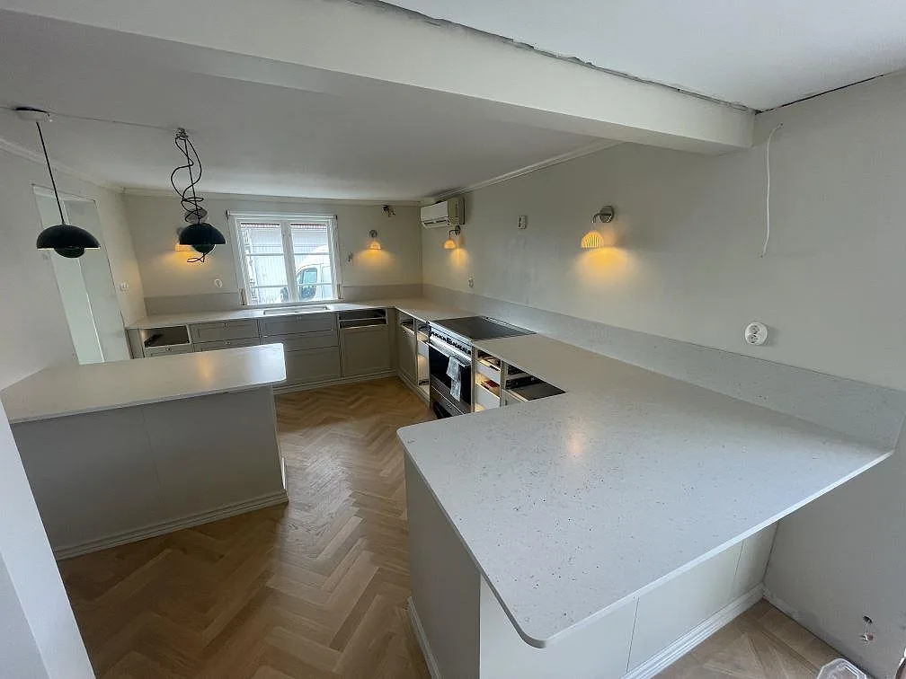 Køkkenbordplade i gräddvit Silestone Lime Delight, mat Mocka, i ett U-format køkken med halvö og herringbone-parkett i Mullsjö, fotograferat under montering.
