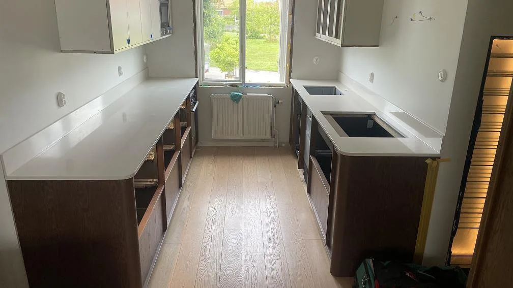 Køkkenbordplade i poleret Silestone Linen Cream komposit med stänkkant, diskhozon og hällöppning i ett køkken i Halmstad.