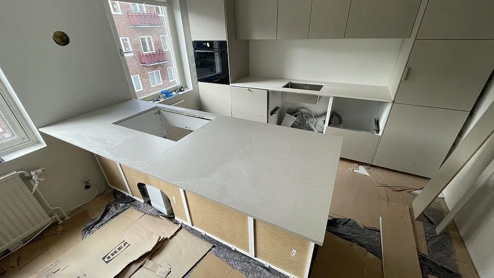 Køkkenbordplade og køkkenø i mat Silestone Linen Cream, 20 mm, under montering i ett ljust køkken i Helsingborg.
