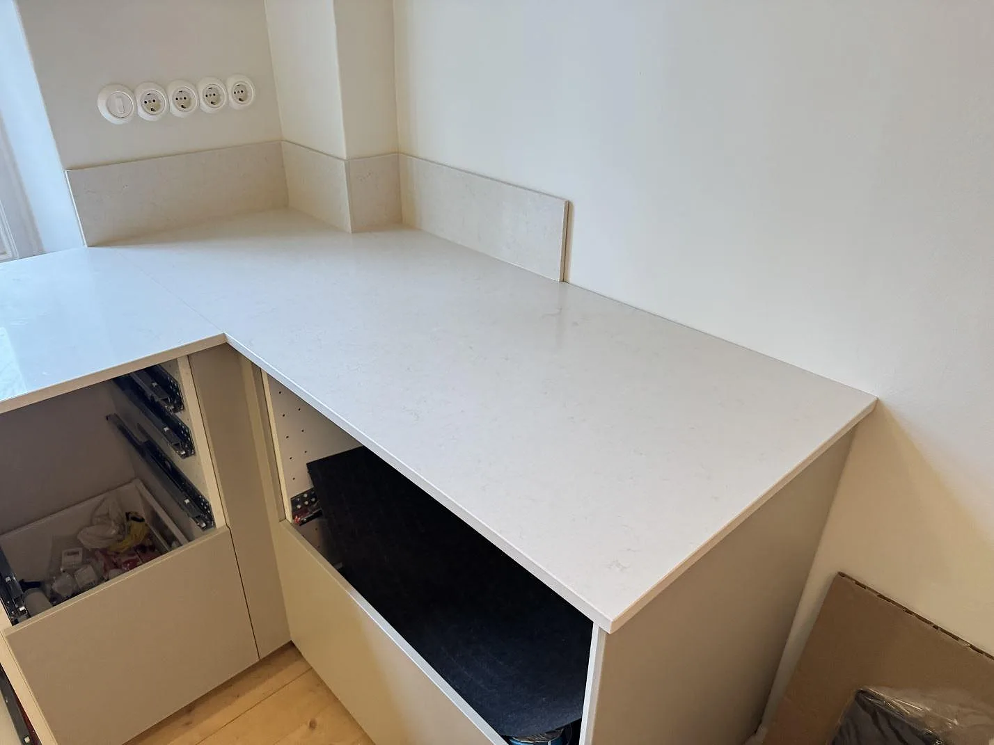 Køkkenbordplade i Silestone Linen Cream, poleret, som vinklar rundt om ett hjørner i L-form med låg stänkkant i ett køkken under montering i Helsingborg.