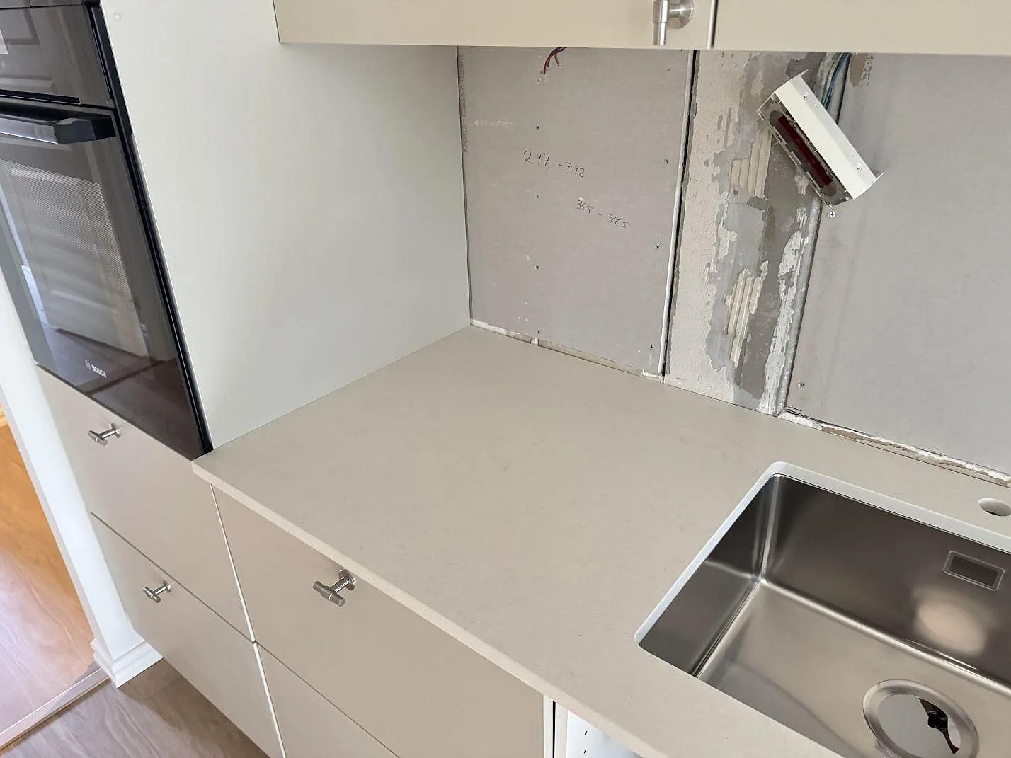 Køkkenbordplade i Silestone Linen Cream, mat krämvit komposit, med underlimmad rostfri vask og bakomliggande oinredd væg i ett køkken under montering i Malmö.