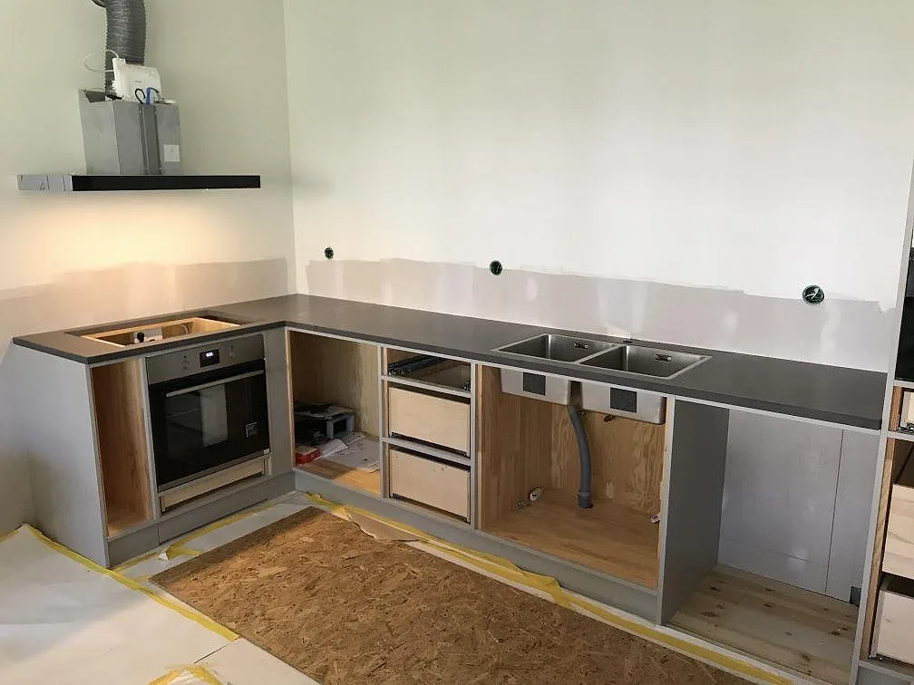 Køkkenbordplade i grå komposit Silestone Merope, mat overflade, med inbyggd ovn og underlimmad rostfri dubbelho i ett L-format køkken under montering i Stenkullen.