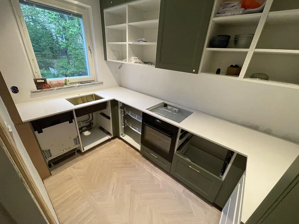 L-formad køkkenbordplade i hvid Silestone Miami White, poleret kvartskomposit, med vask og hällurtag i ett køkken i Bromma under montering.