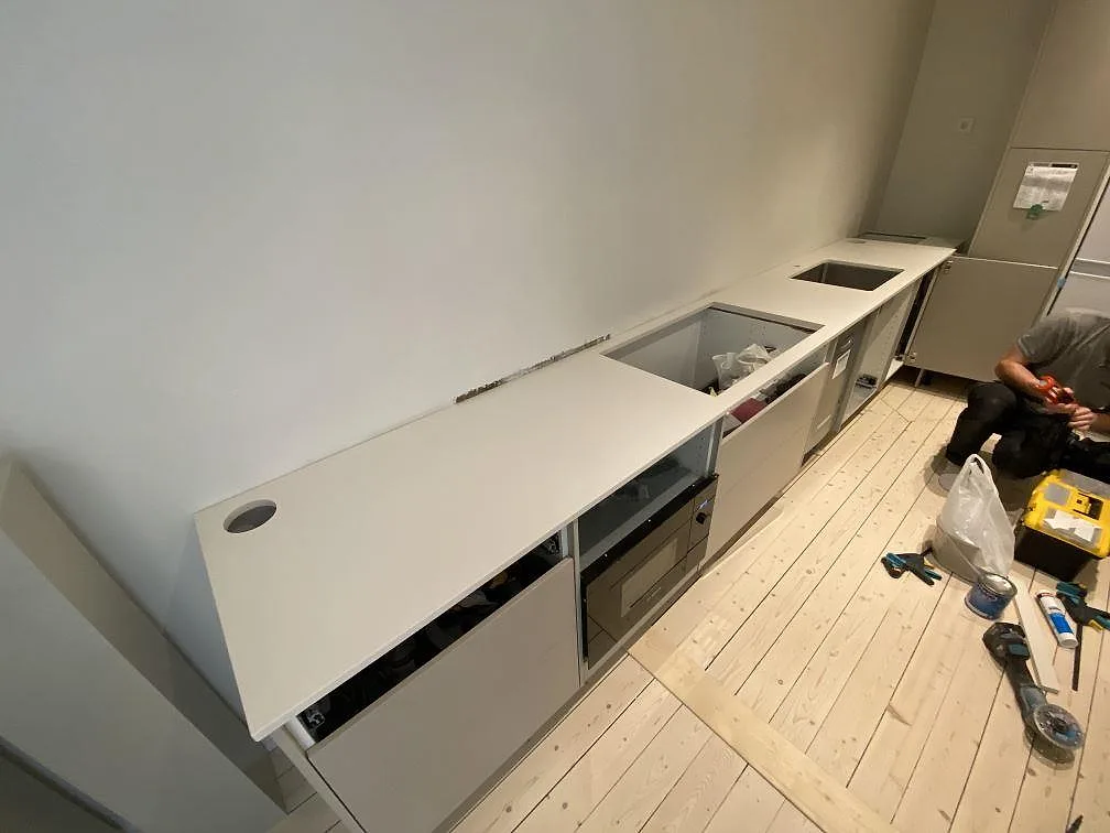 Køkkenbordplade i hvid Silestone Miami White, poleret, längs en lang væg med underlimmad rostfri vask i ett køkken under montering i Malmö.