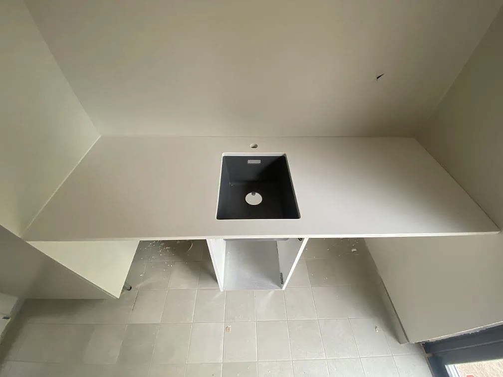 Køkkenbordplade i hvid Silestone Miami White, poleret, med underlimmad sort kompositdiskho i ett køkken under montering i Ramdala.
