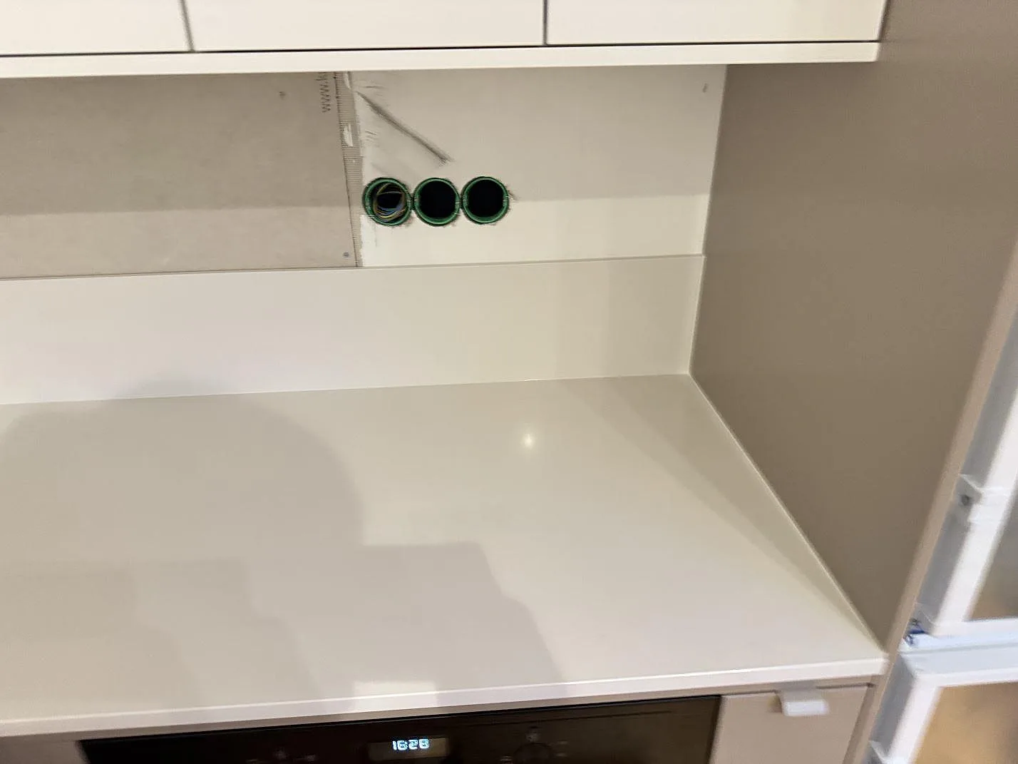 Køkkenbordplade i poleret Silestone Miami White med hvid stänkkant under väggskåp i ett køkken i Växjö.