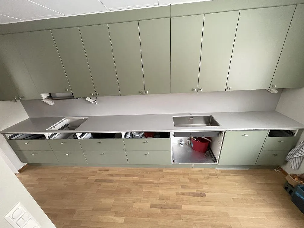 Køkkenbordplade i ljusgrå Silestone Motion Grey, mat 20 mm, med underlimmad rostfri vask og tom hultagning for kogeplade i ett køkken med salviegröna fronter i Älvsjö.