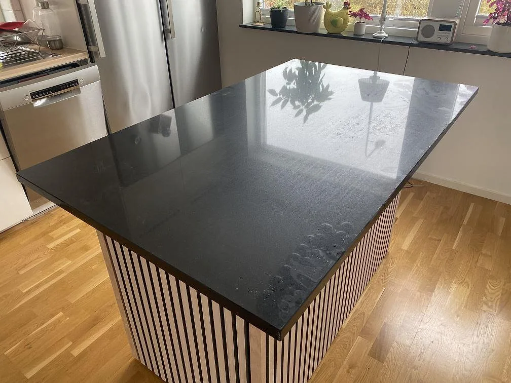 Køkkenø med Bordplade i sort, poleret Silestone Negro Tebas, monteret på en randig östomme i ett ljust køkken med ekparkett i Lund.