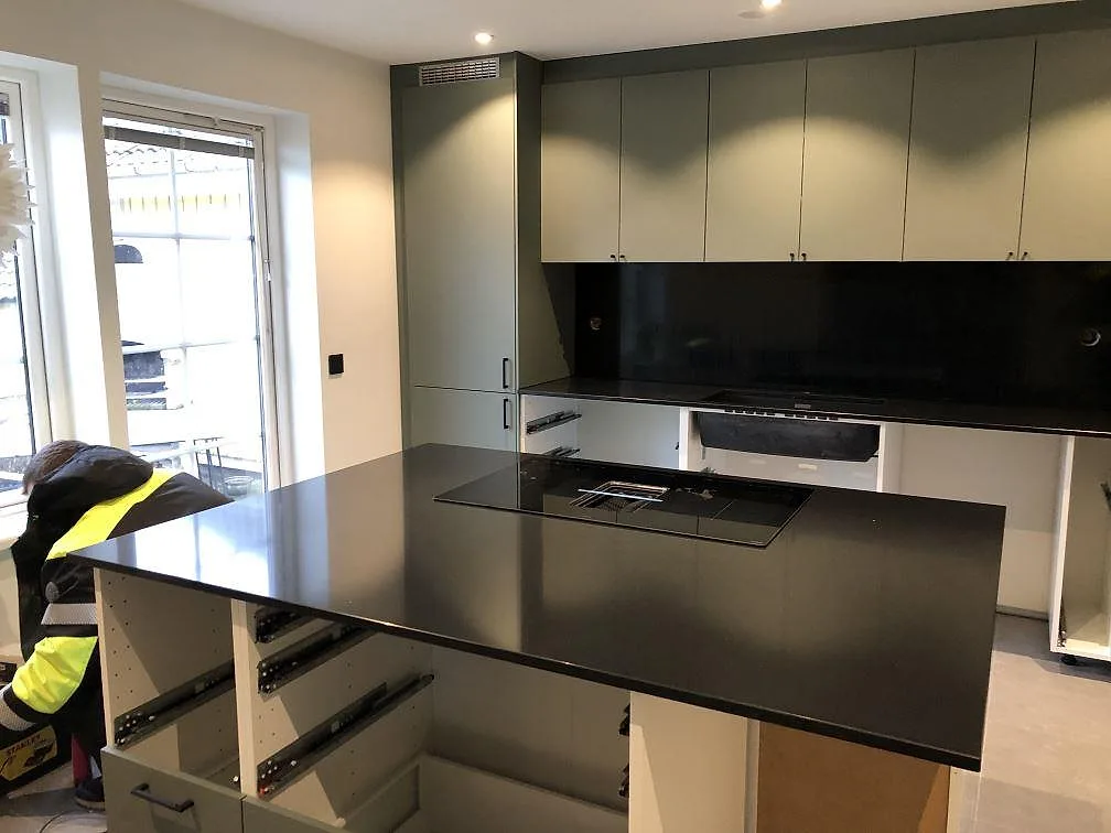 Køkkenbordplade og køkkenø i sort Silestone Negro Tebas, poleret, med övermonterad induktionshäll i ett køkken under montering i Svedala.